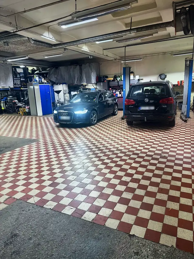 Verkstadsgolvet med rött och vitt rutigt klinker, en Audi A6 och en Volkswagen Sharan inne för service